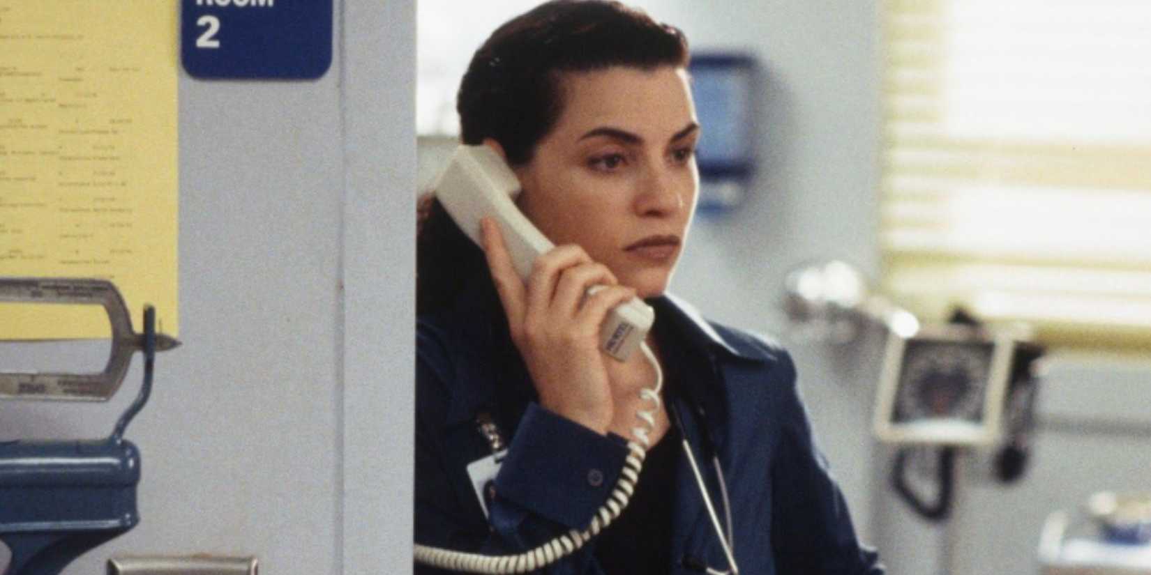 Carol (Juliana Margulies) ao telefone, uma expressão sombria no rosto no pronto-socorro