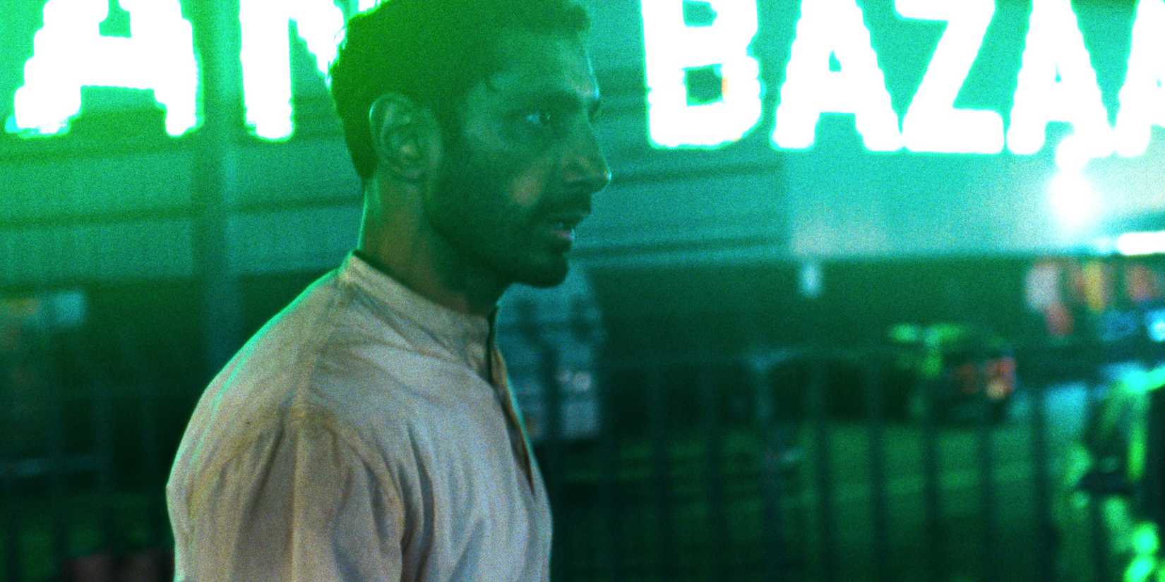 Riz Ahmed walking down a neon-drenched street in Hamlet 2025