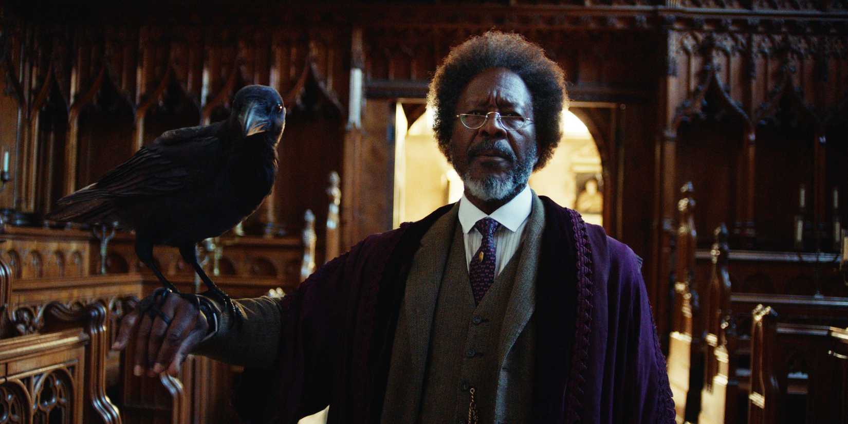 Clarke Peters como o dæmon Dr Carne em His Dark Materials, segurando seu dæmon em forma de corvo.