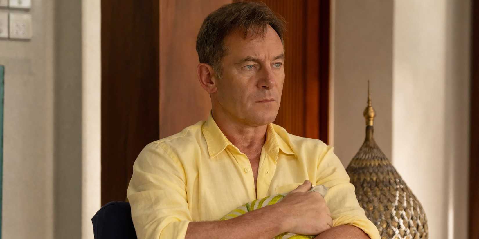 Jason Isaacs como Timothy segurando um travesseiro e parecendo distraído sentado em uma cadeira na 3ª temporada de The White Lotus