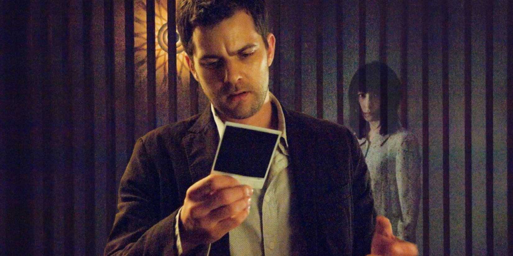 Joshua Jackson as Ben looks at a photo as a ghost stands behind him in Shutter