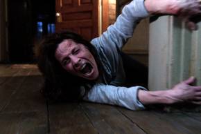 Lili Taylor as Carolyn screaming while holding onto a door frame in The Conjuring