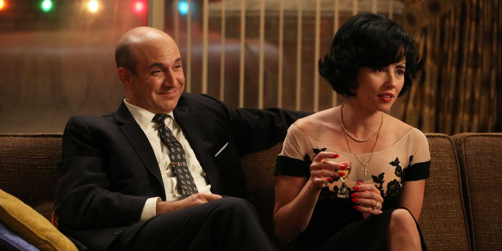 Arnold Rosen (Brian Markinson) and Sylvia (Linda Cardellini) sitting and laughing on a couch on Mad Men.