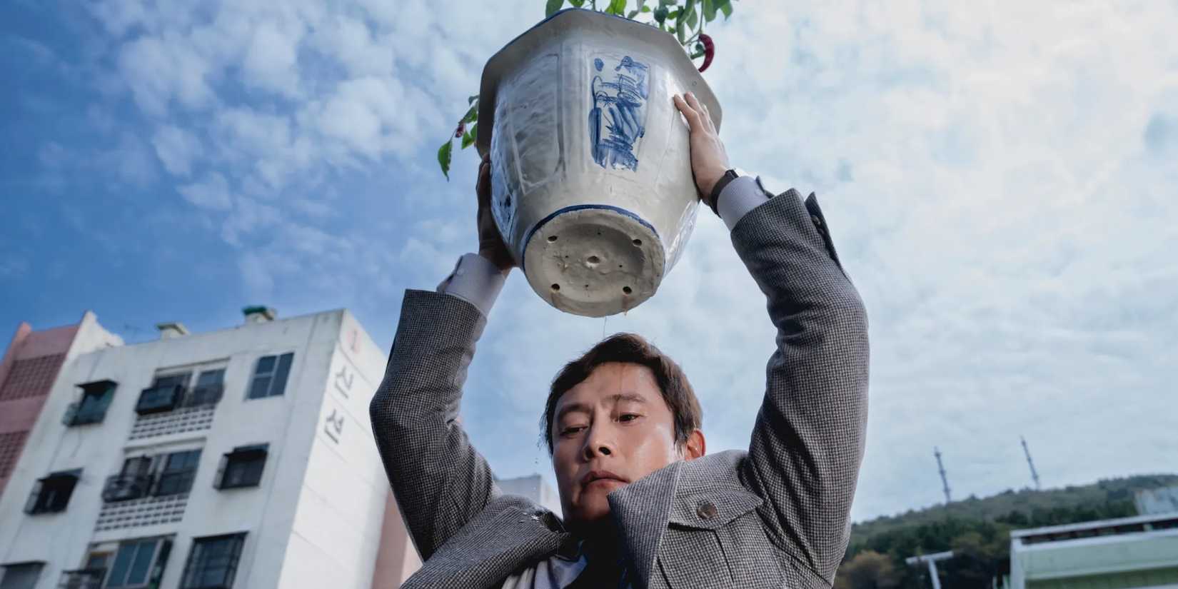 Man-su holds a potted plant over the edge of the building in No Other Choice