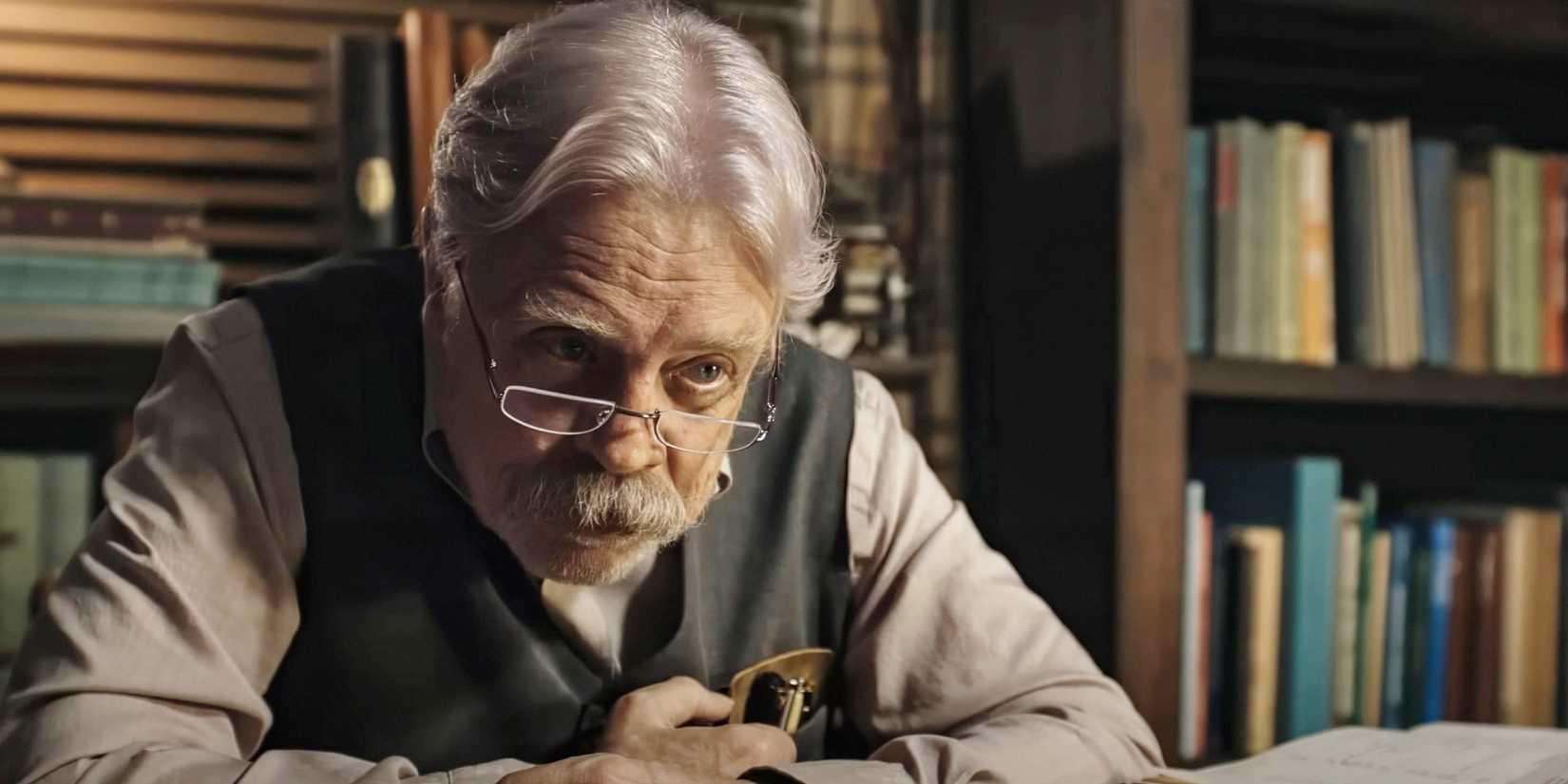 Mark Hamill sits at a desk peering over his glasses while engaged in conversation in a scene from The Life of Chuck.