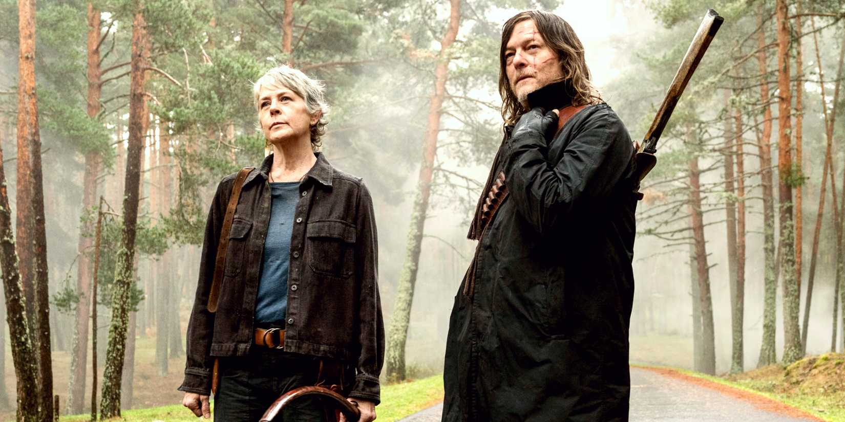 Melissa McBride holding a bow and Norman Reedus with a rifle over his shoulder standing on a road within a forest in Daryl Dixon season 3