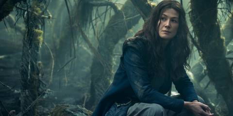 Rosamund Pike kneeling among trees as Moiraine In The Wheel Of Time