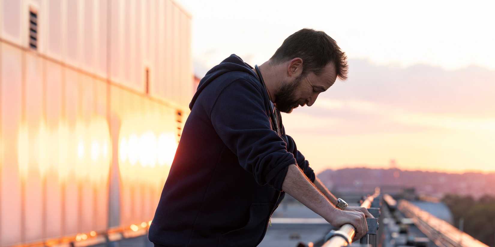 Noah Wyle as Dr. Robby leaning on a balcony railing in The Pitt