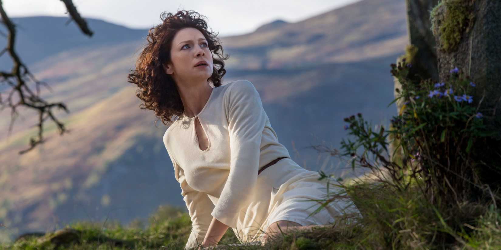Claire Fraser (Caitríona Balfe) chocada no chão em Outlander.