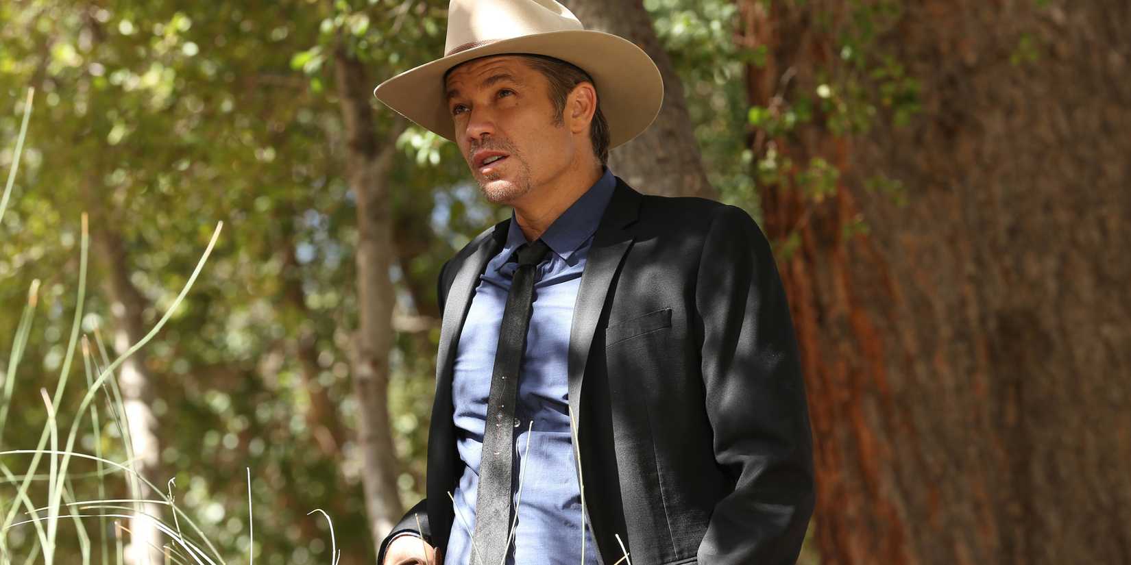 Timothy Olyphant como Raylan Givens em pé do lado de fora, sério, em Justified