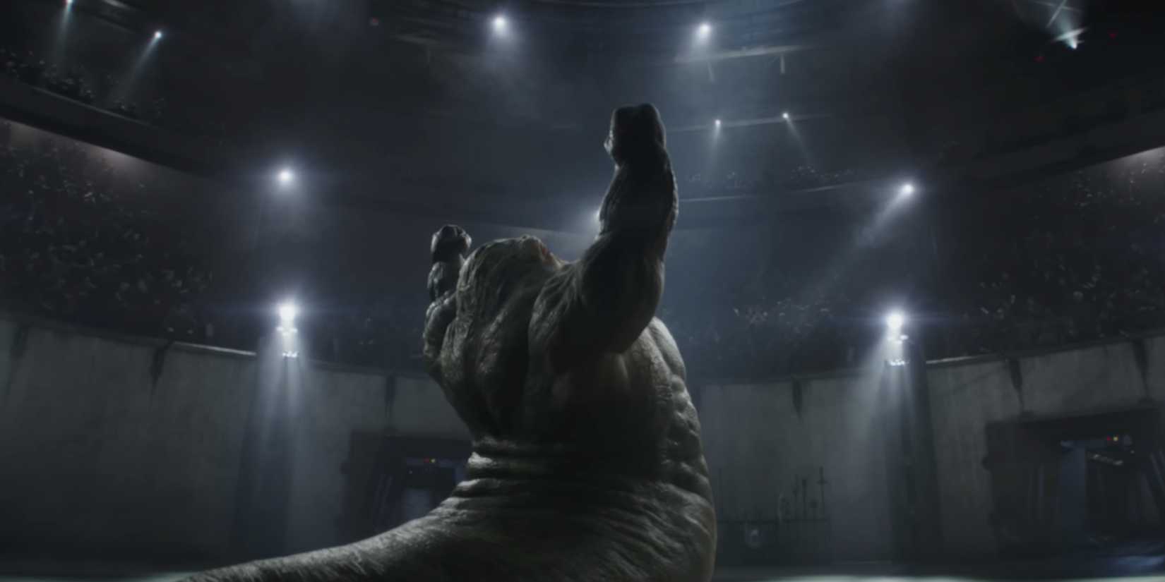 Rotta the Hutt throws his fists into the air in victory at the center of a fighting ring.