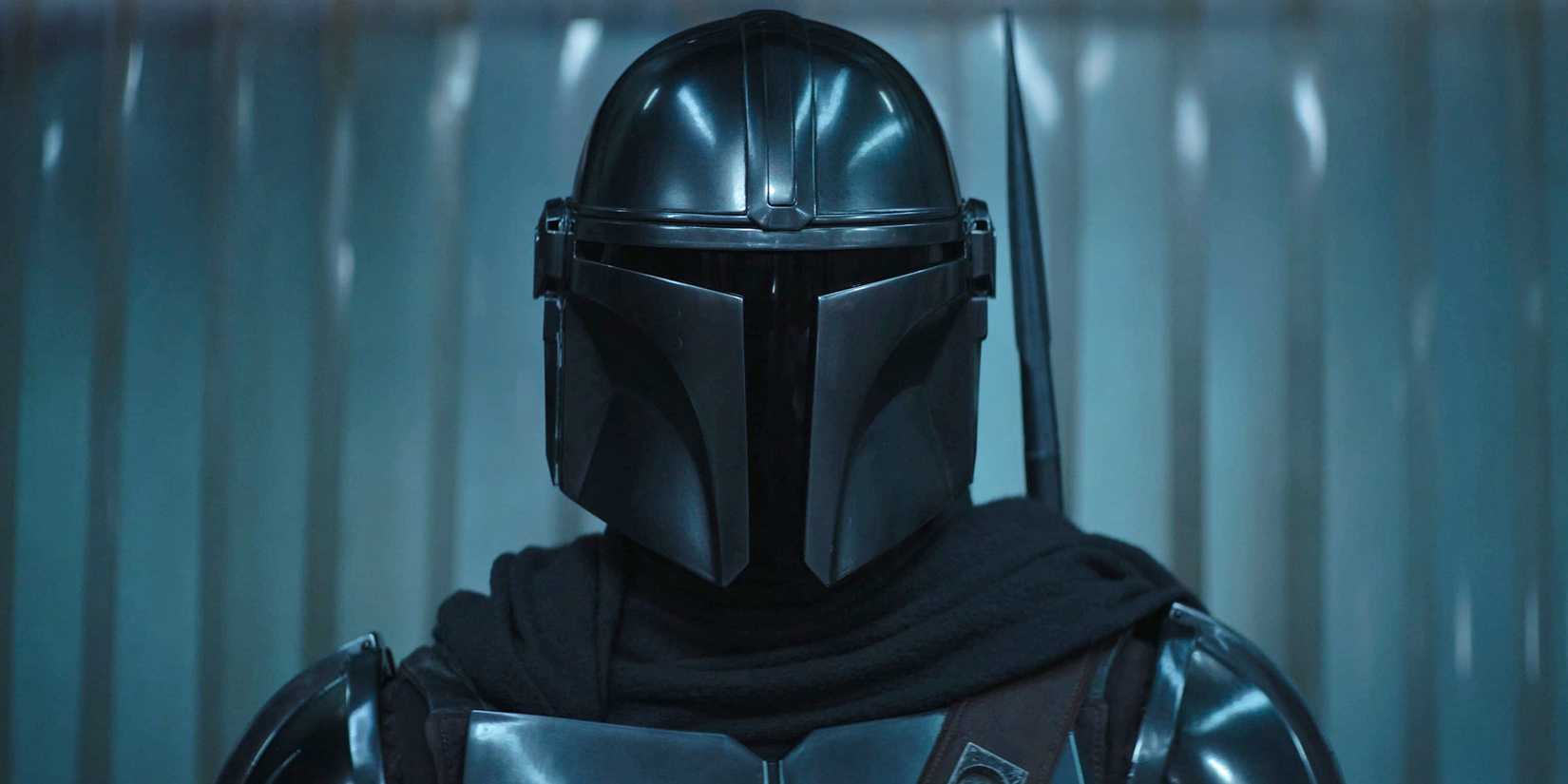 Din Djarin, wearing a helmet, enters from above his shoulders and looks around the room.