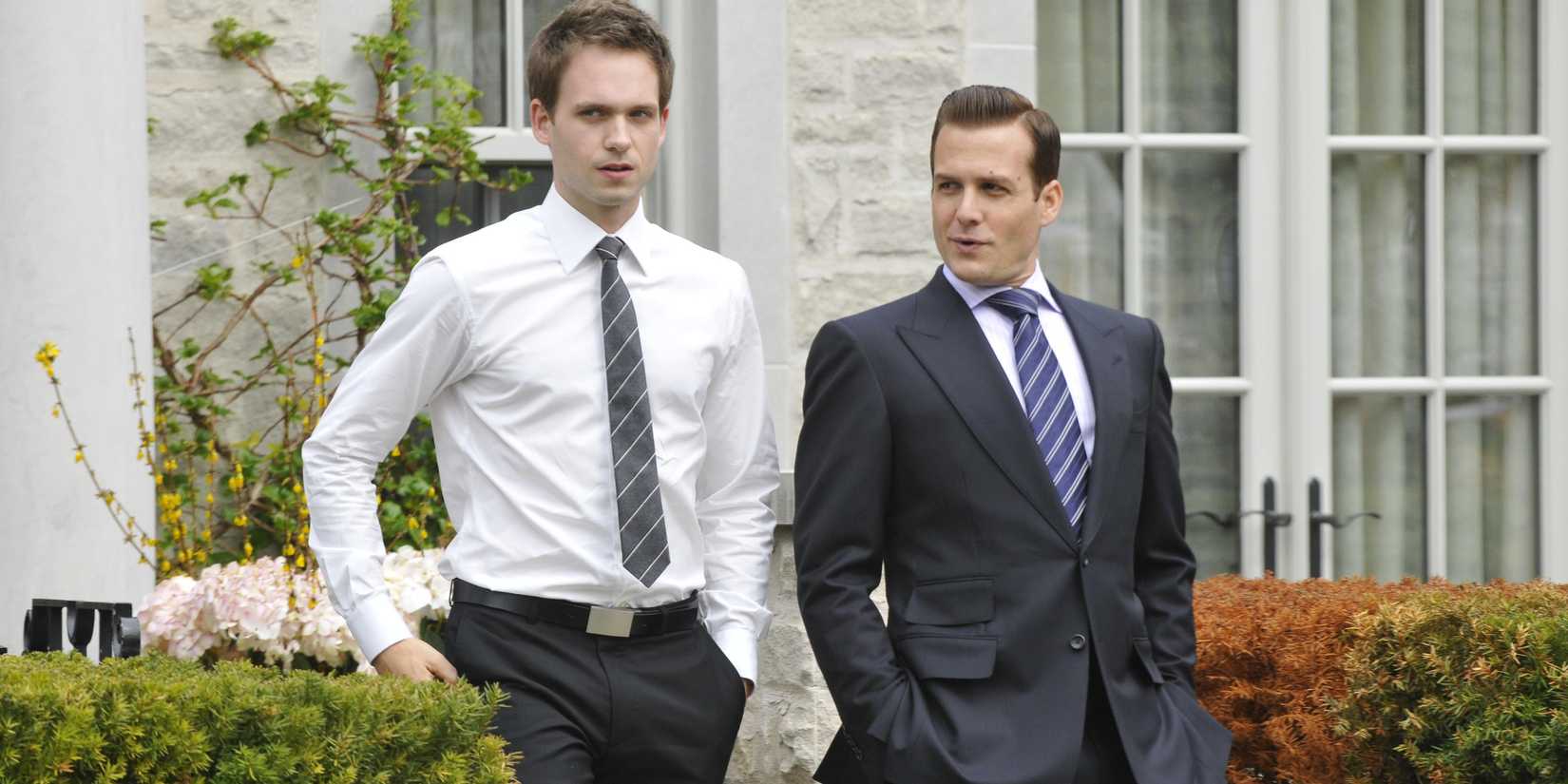 Patrick J. Adams and Gabriel Macht walking side-by-side near bushes in Suits