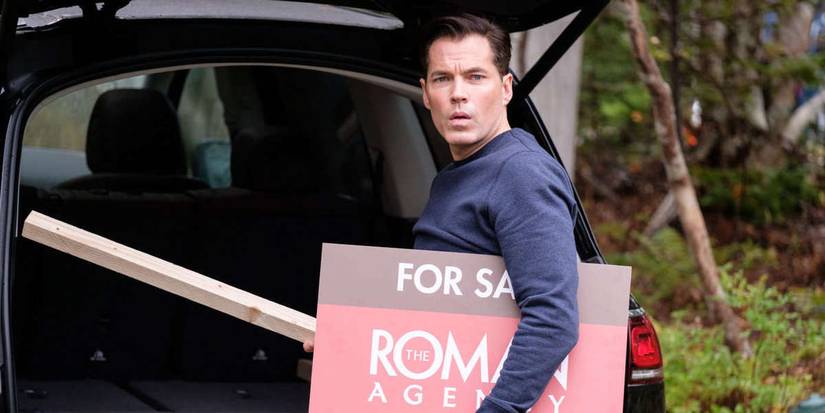 SurrealEstate Luke holding a 'for sale' sign outside his car and looking surprised