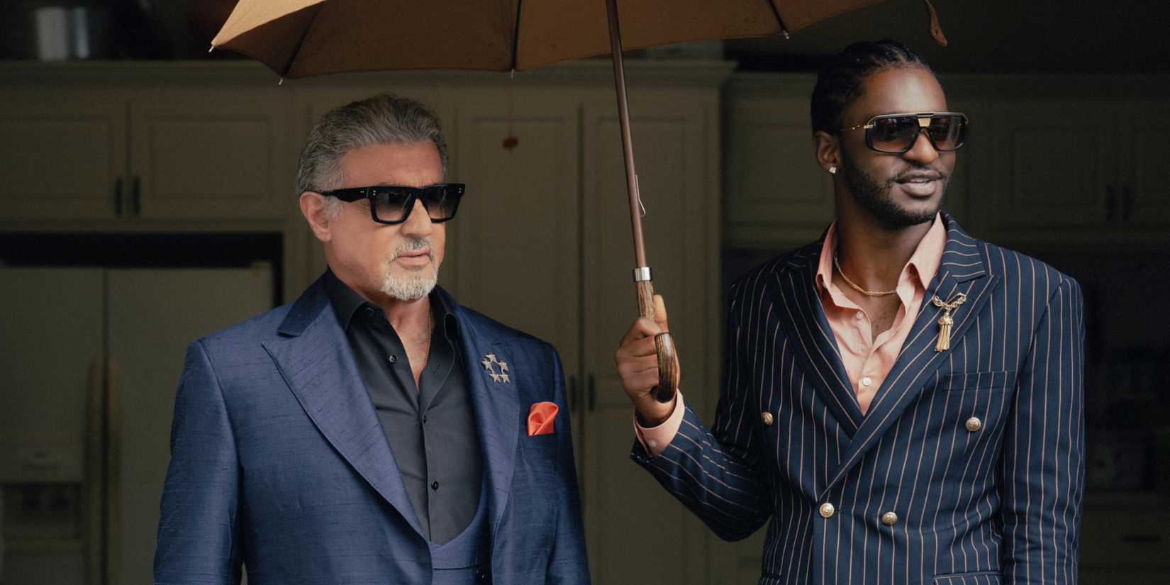 Sylvester Stallone as Dwight Manfredi next to Jay Will as Tyson Mitchell holding an umbrella in Tulsa King season 3