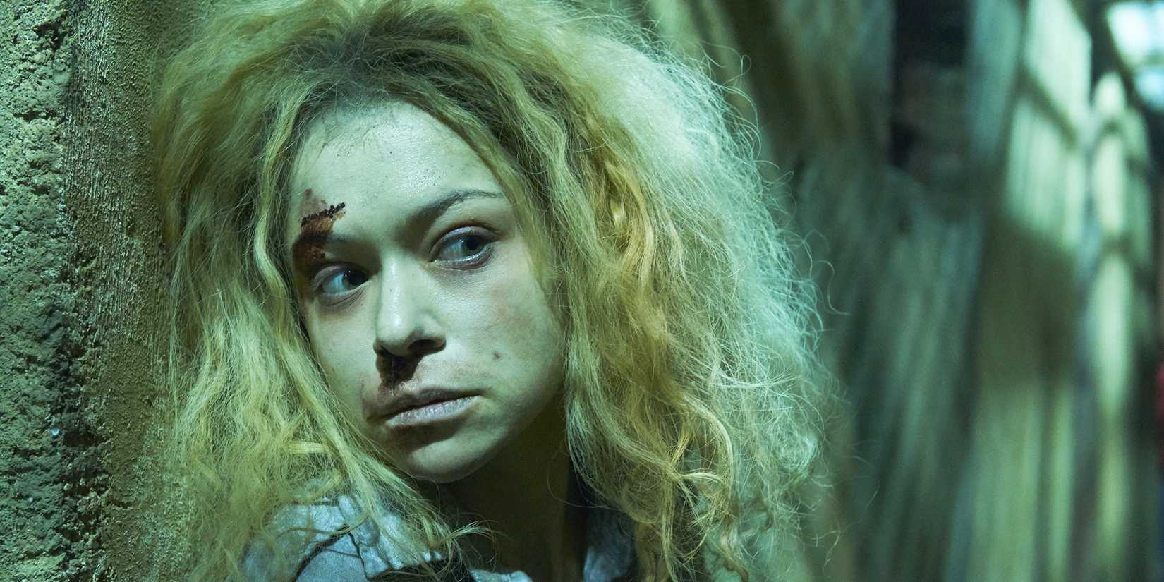 Tatiana Maslany looking nervous around a corner with blonde hair in Orphan Black