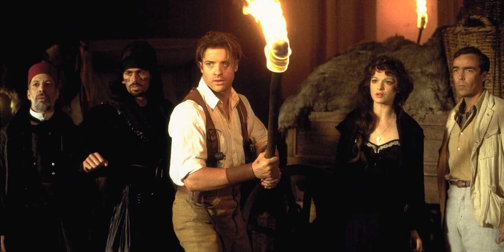 Brendan Fraser segura uma tocha dramaticamente em frente ao elenco de A Múmia: O Retorno.
