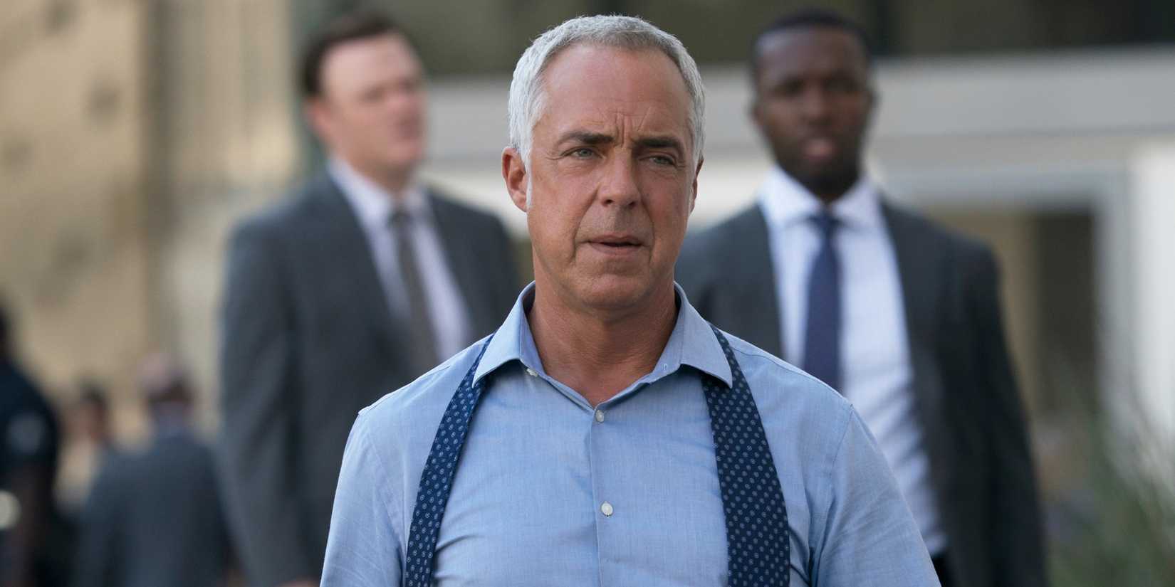 Titus Welliver in an episode of Bosch, looking off-camera, while holding his coat and tilting his head