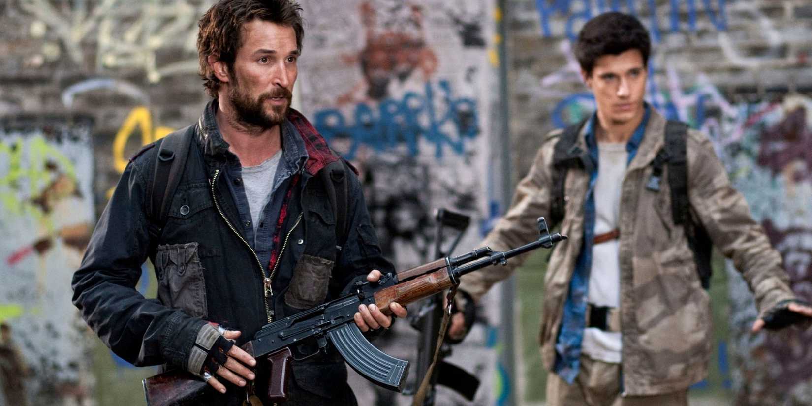 Tom Mason segurando um rifle de assalto com Hal Mason segurando as mãos para cima ao fundo, em Falling Skies
