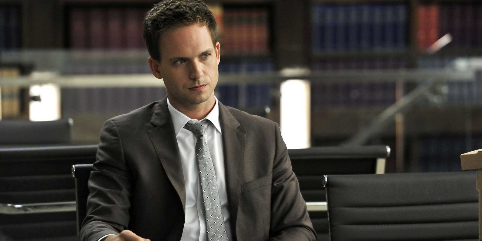 Patrick J. Adams as Mike Ross sitting in a library, deep in thought as he stares across the room, in Suits.