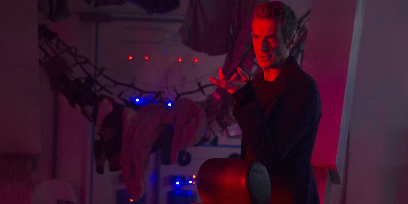 The Twelfth Doctor looking confused as he holds his hand out while standing in a room filled with red light in the Doctor Who episode “Listen.”