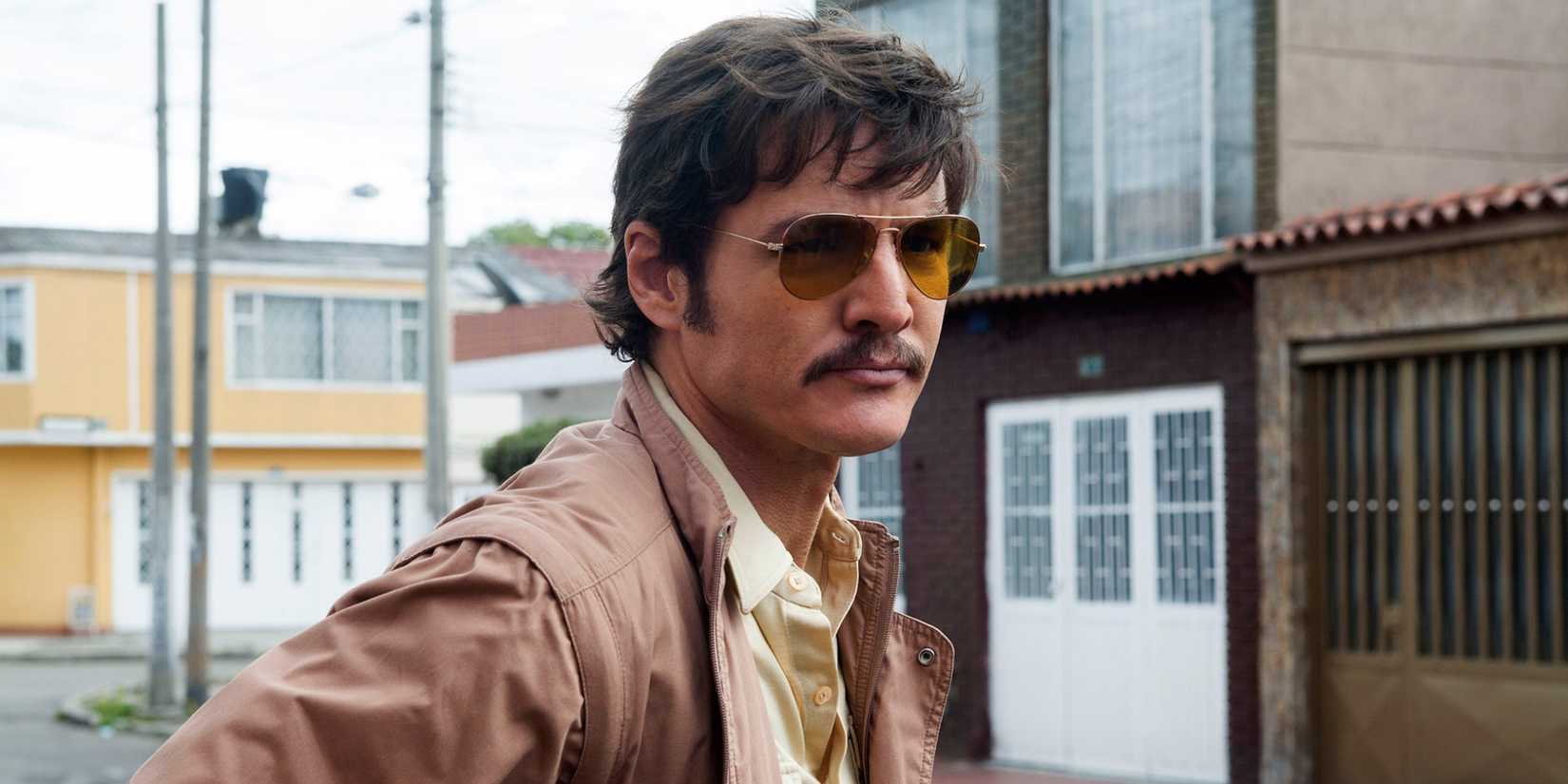 Pablo Escobar standing in the street, wearing sunglasses and staring off at something, in Narcos.