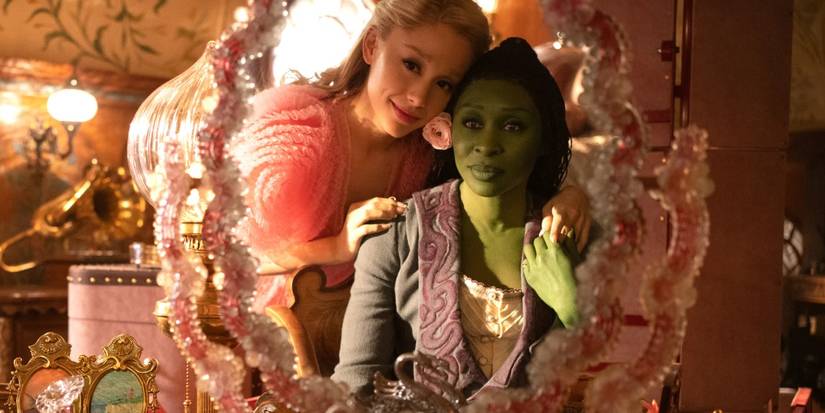 Glinda e Elphaba de mãos dadas, olhando no espelho em seu quarto em Wicked.
