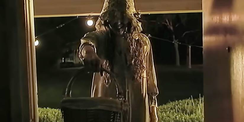 A creepy trick or treater holds out a basket in a doorway in V/H/S/Halloween