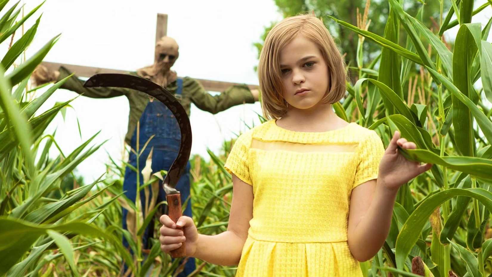 A killer child holding a sickle near a scarecrow in Children of the Corn Runaway