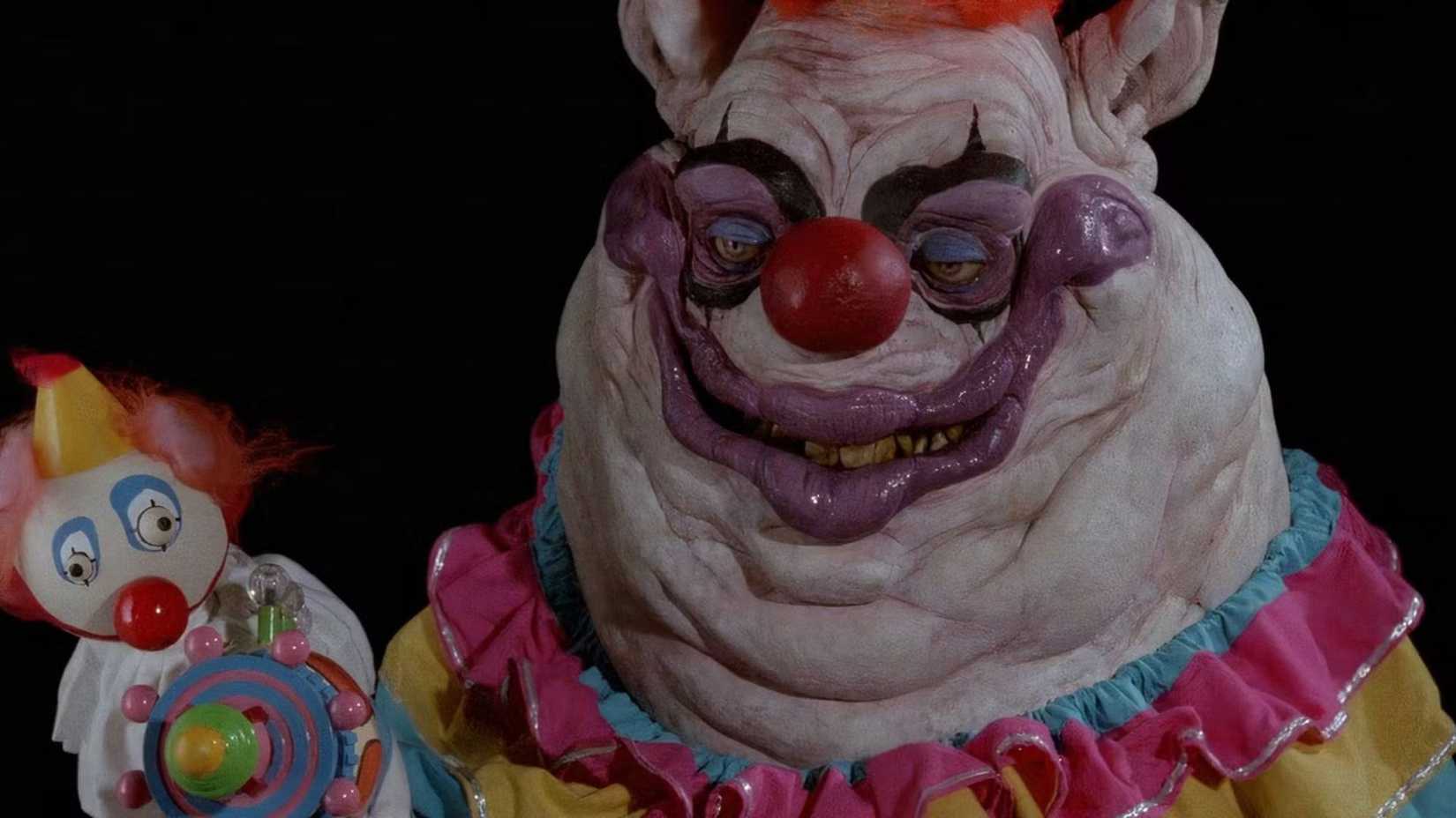 An alien clown smiling with little doll in Killer Klowns from Outer Space