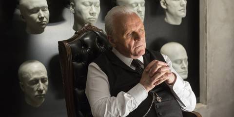 Anthony Hopkins as Dr. Robert Ford in Westworld, deep in thought sitting in a chair, head molds of the park's hosts hung on the wall behind him