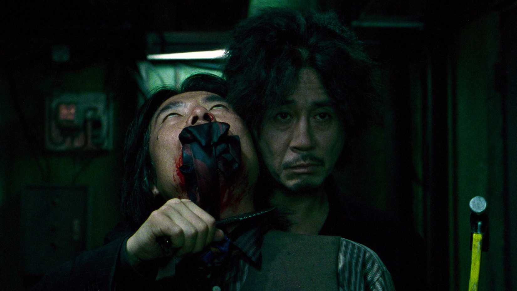 A man holds a knife to a gagged man's throat in Oldboy