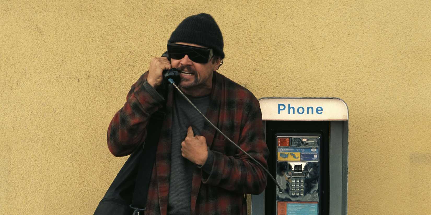 Bob angrily yelling into a payphone while pointing at his own chest in One Battle After Another
