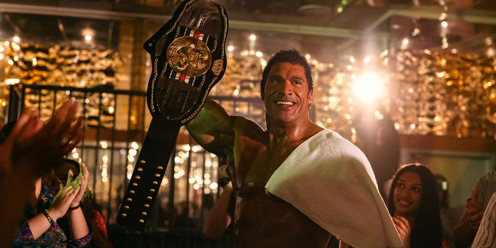 Dwayne Johnson as Mark Kerr holding up a championship belt in The Smashing Machine