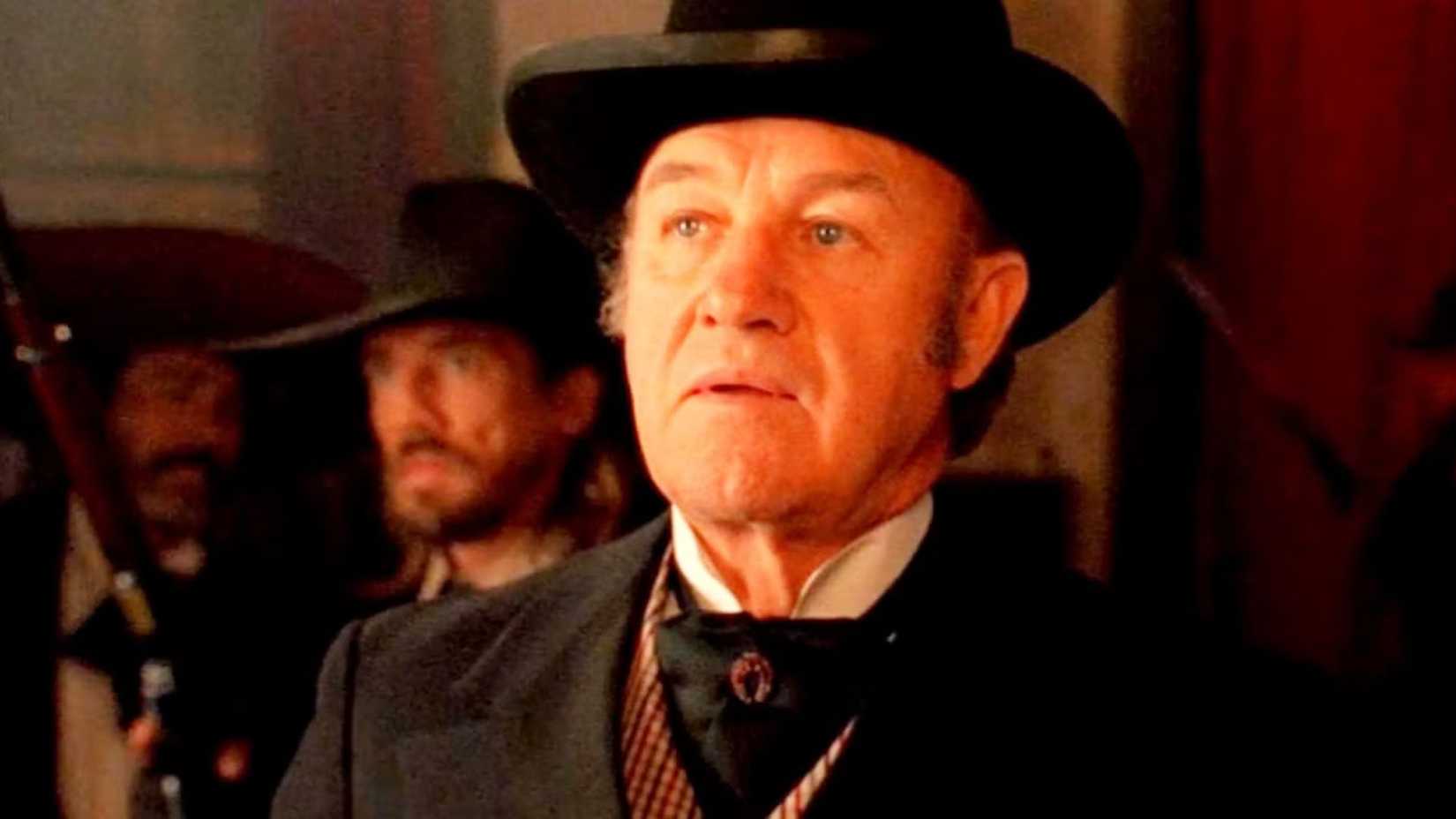 Gene Hackman, como John Herod, parece surpreso ao ouvir más notícias na frente de um grupo de homens em The Quick and the Dead