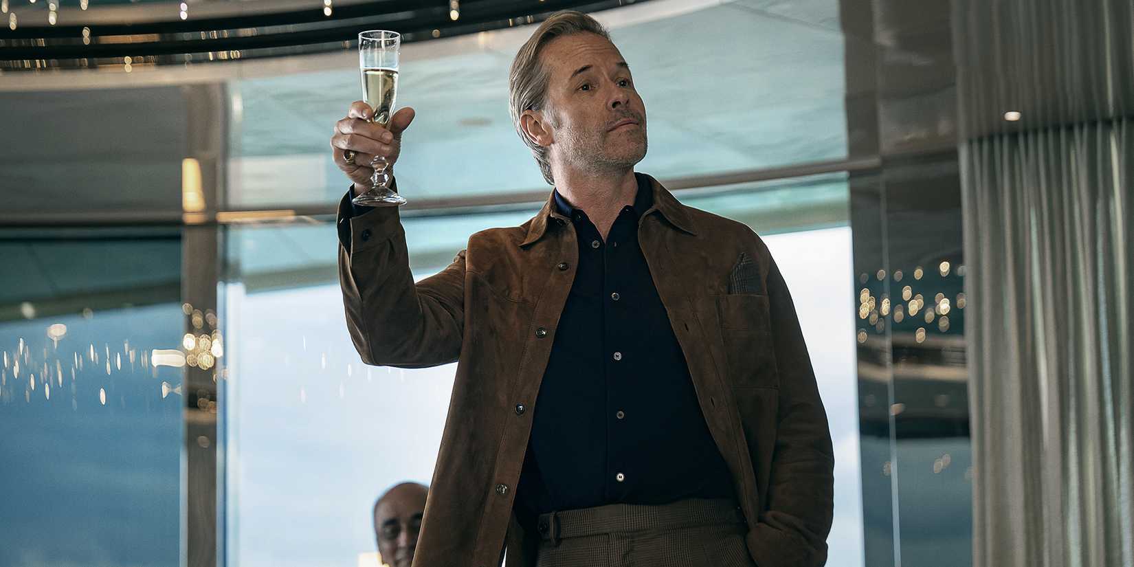 Guy Pearce as Richard holding a champagne glᴀss up for a toast in The Woman in Cabin 10