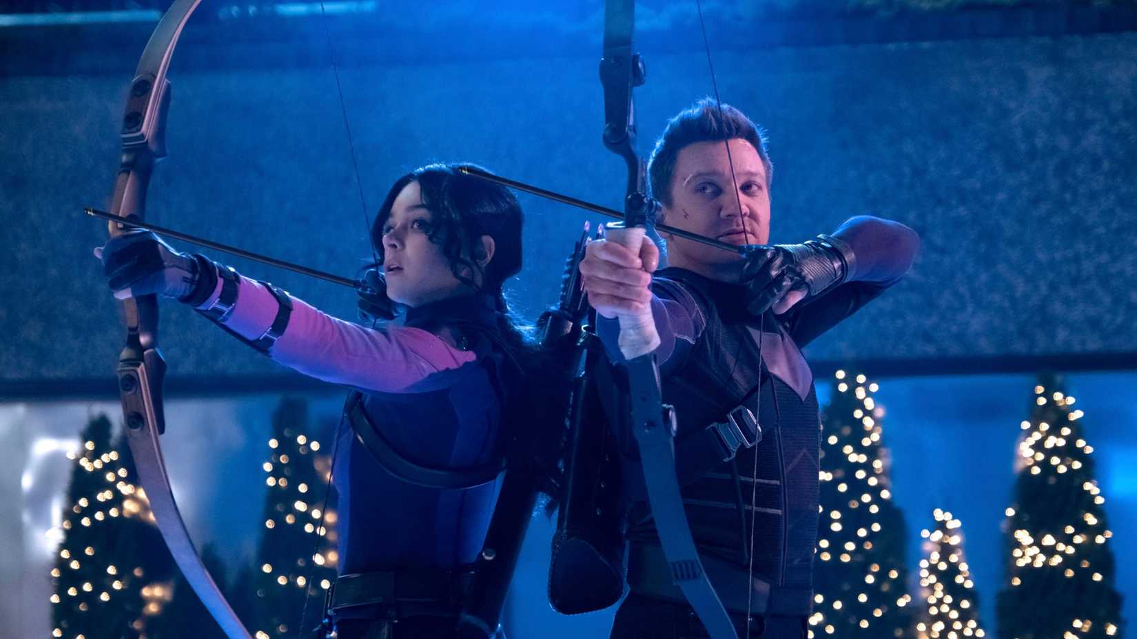 Hailee Steinfeld como Kate Bishop e Jeremy Renner como Clint Barton segurando arcos e flechas em uma pista de gelo em Hawkeye