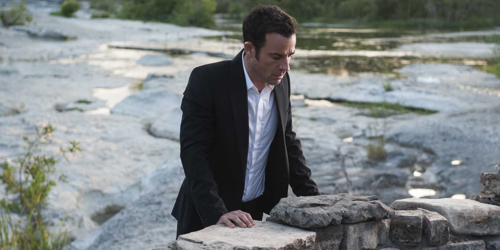 Kevin em pé contra uma parede de pedra em The Leftovers.