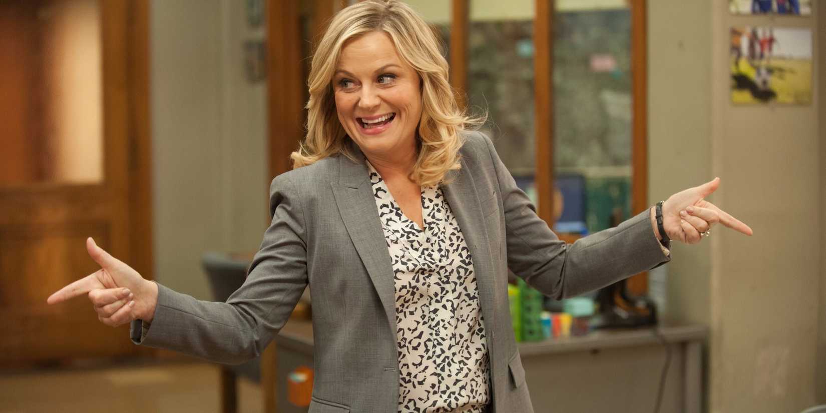Leslie Knope fazendo 'finger guns' e sorrindo no escritório em Parks and Rec.