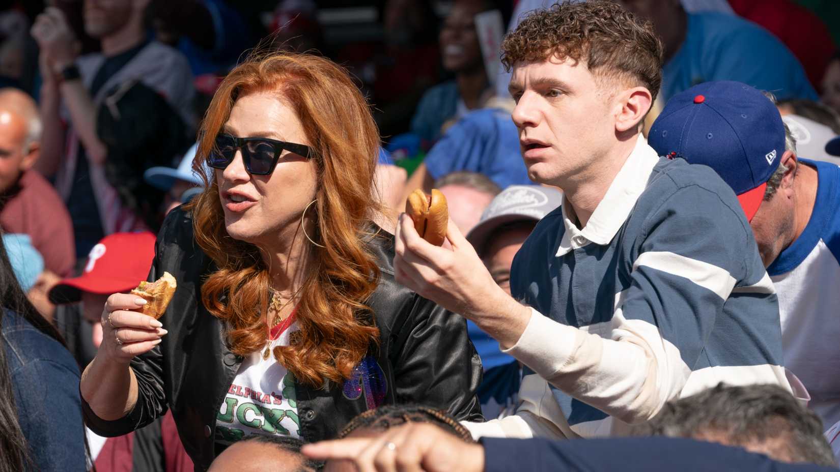 Melissa (Lisa Ann Walter) e Jacob (Chris Perfetti) comendo cachorros-quentes em um jogo esportivo em Abbott Elementary