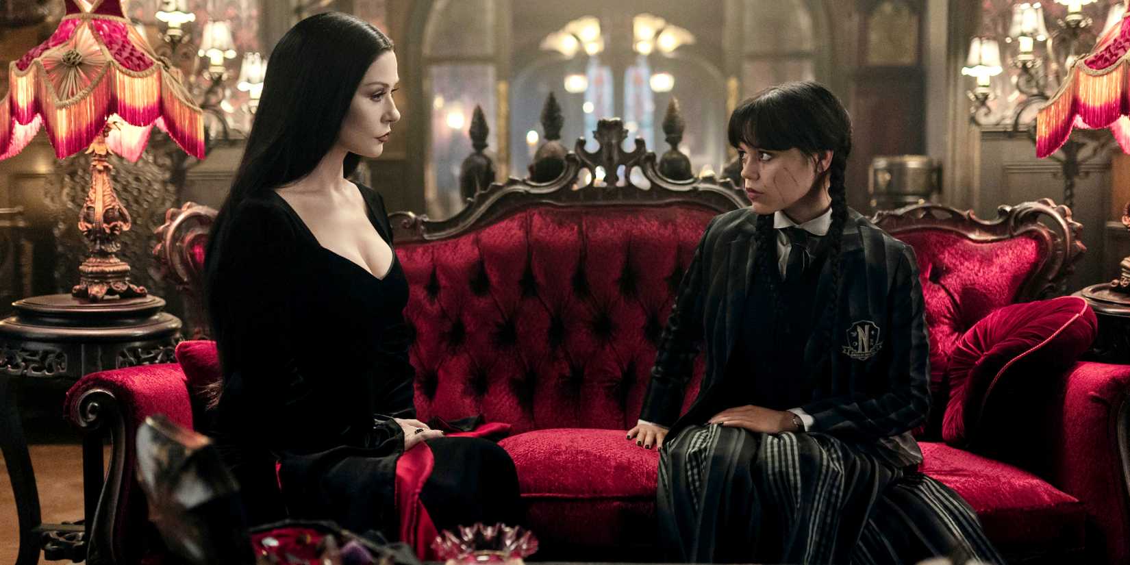 Morticia (Catherine Zeta-Jones) and Wednesday (Jenna Ortega) on a sofa taking in Wednesday season 2