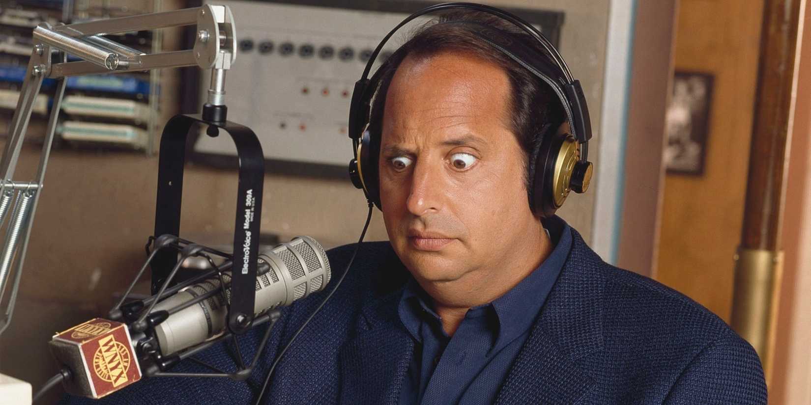 Max (Jon Lovitz) looking concerned with something while speaking on a microphone in NewsRadio.
