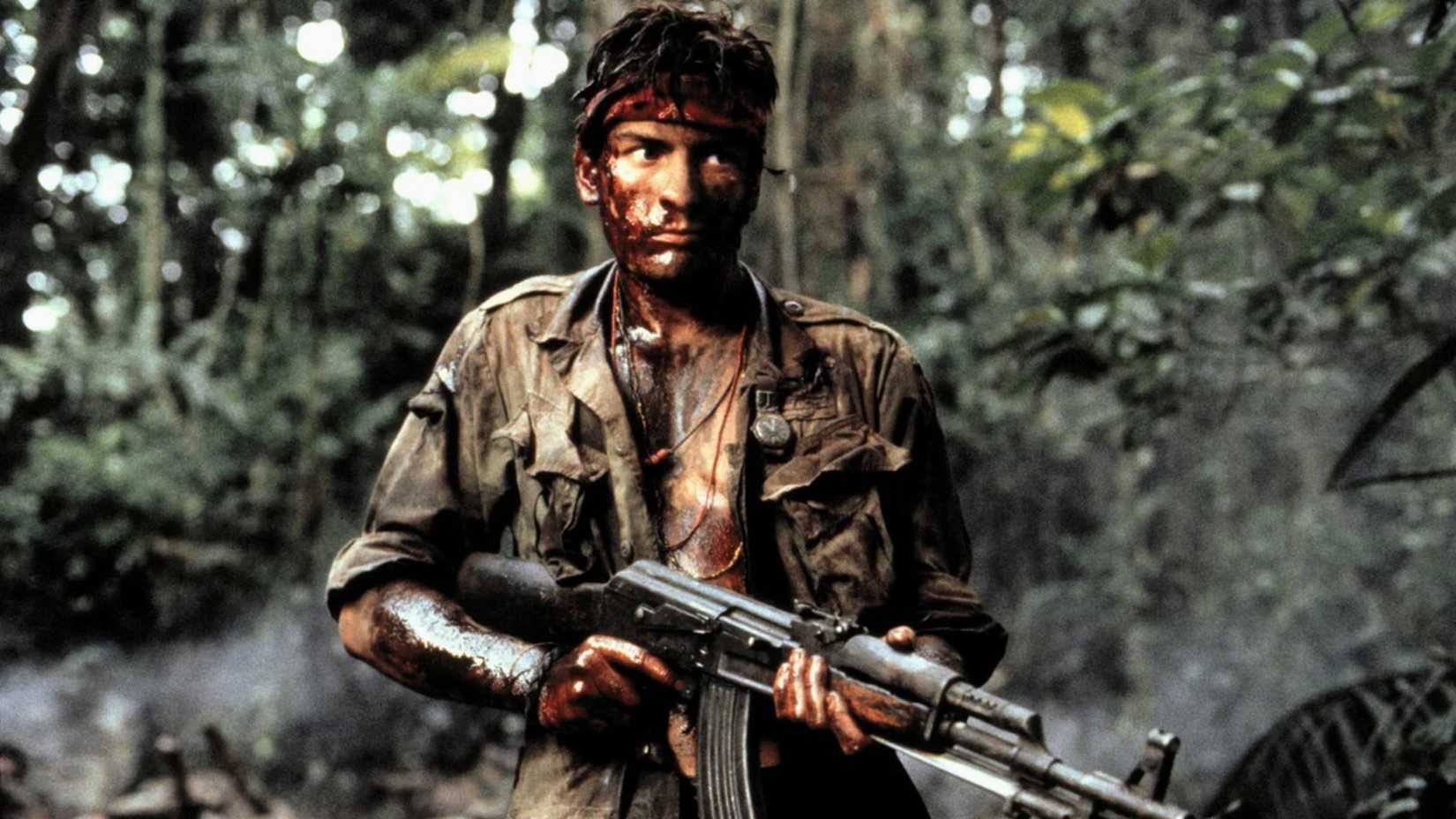 Charlie Sheen stands with a gun while covered in blood and dirt in Platoon