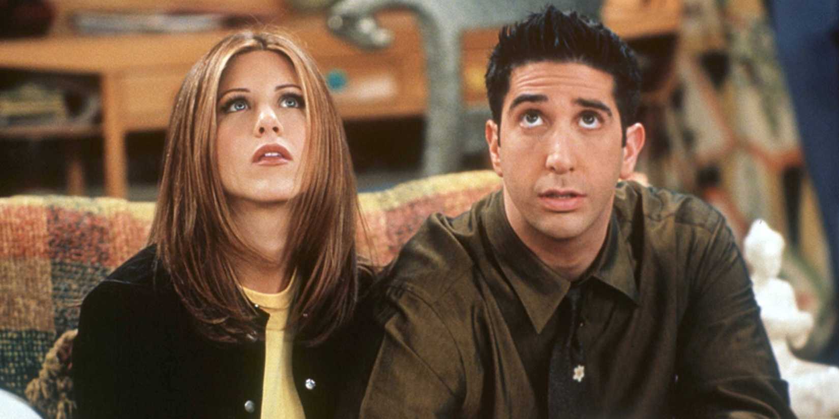 Rachel Green (Jennifer Aniston) e Ross Geller (David Schwimmer) sentados em um sofá olhando para cima em Friends.