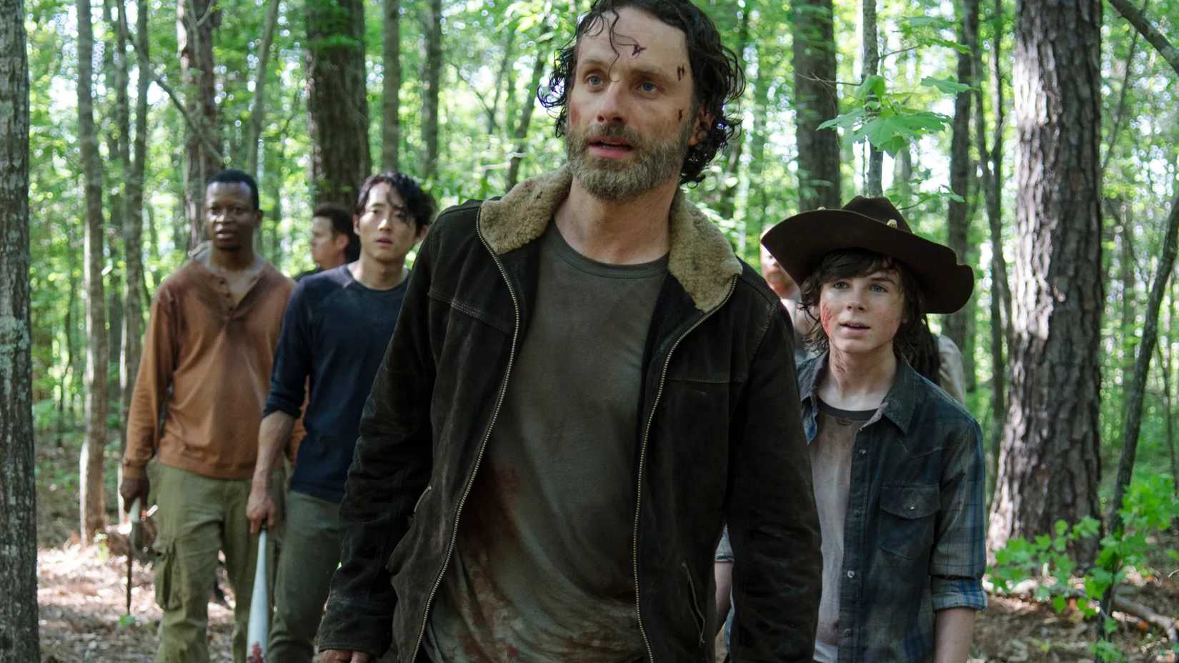 Rick Grimes liderando sobreviventes por uma floresta em The Walking Dead