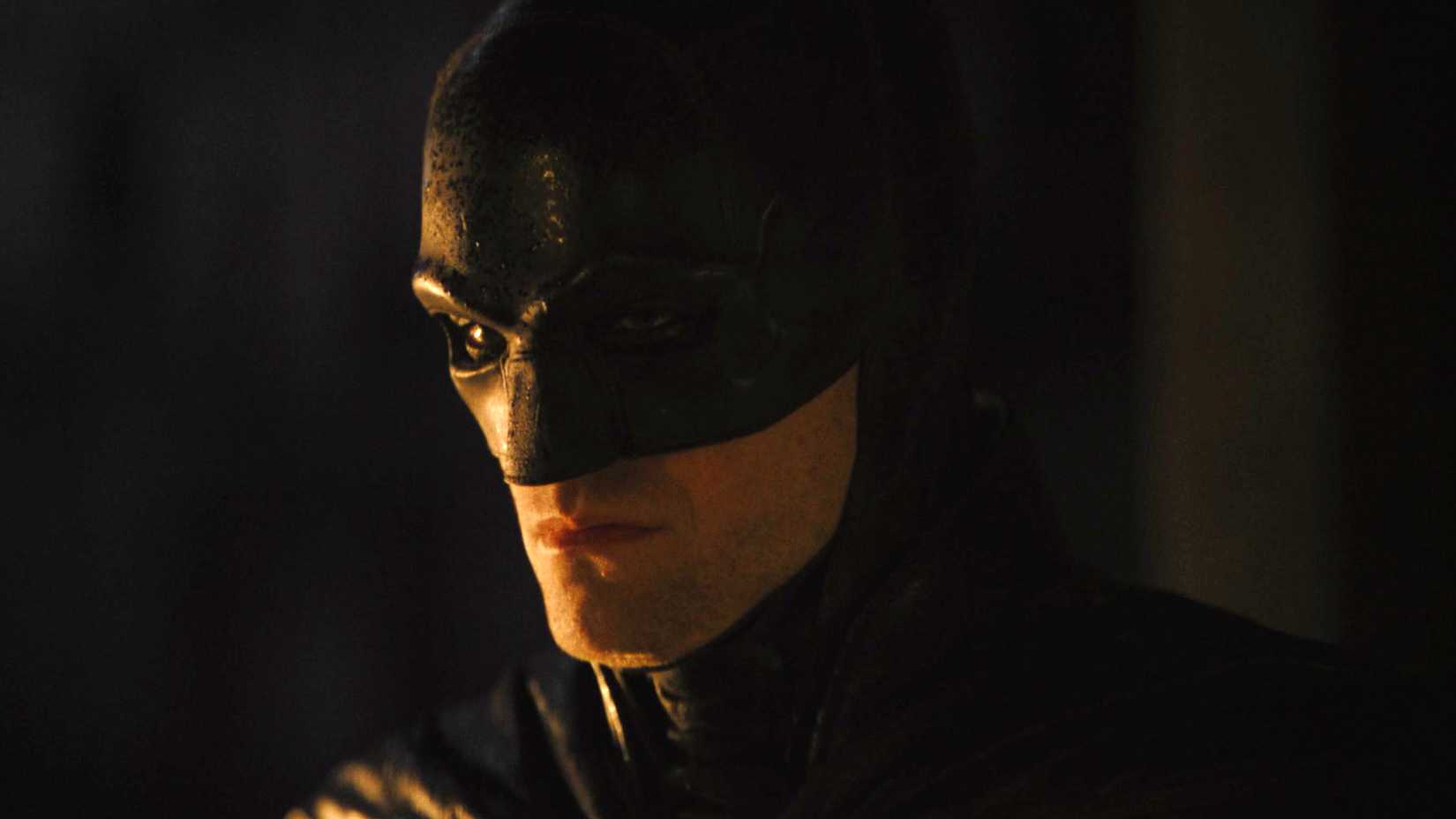 Robert Pattinson como Batman, pensativo em meio às sombras em The Batman.