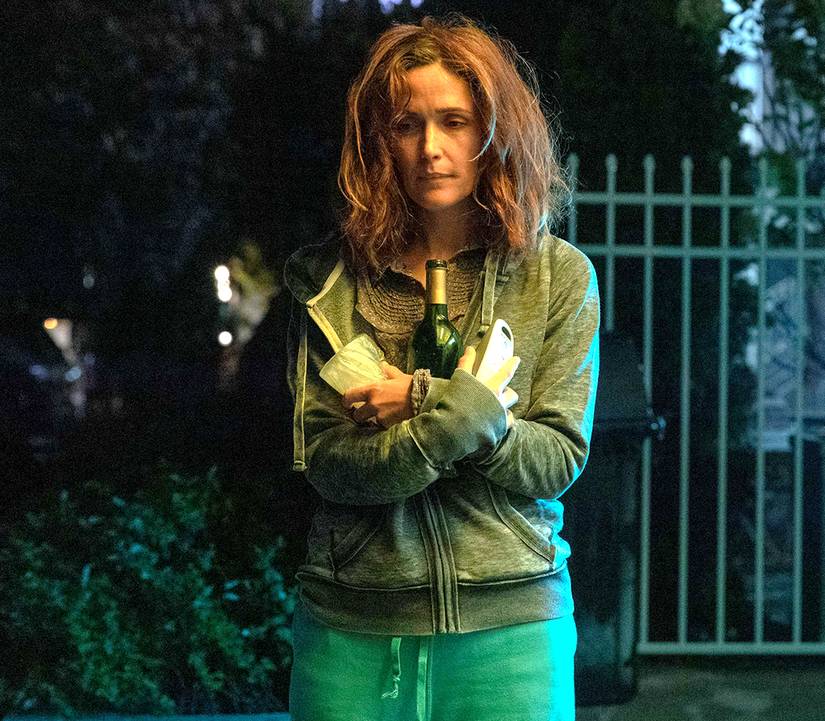 Rose Byrne's Linda looking distraught and holding a bottle of wine and cup while outside in If I Had Legs, I'd Kick You