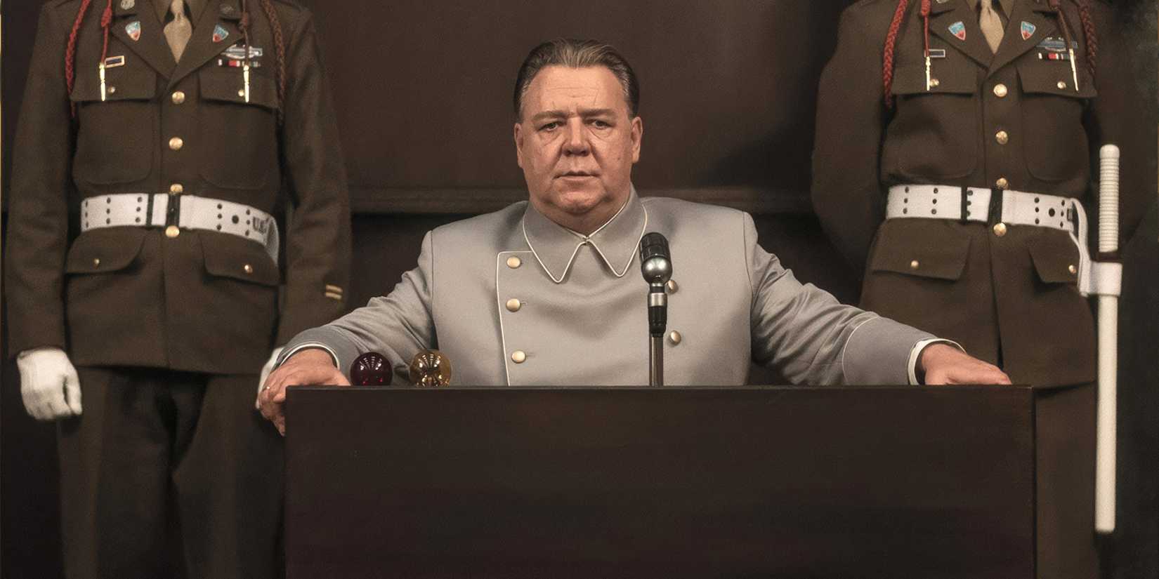 Russell Crowe stares intently forward while on trial flanked by guards in a scene from Nuremberg