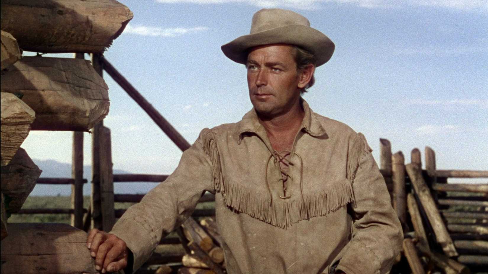 Alan Ladd leans against a post while listening in Shane