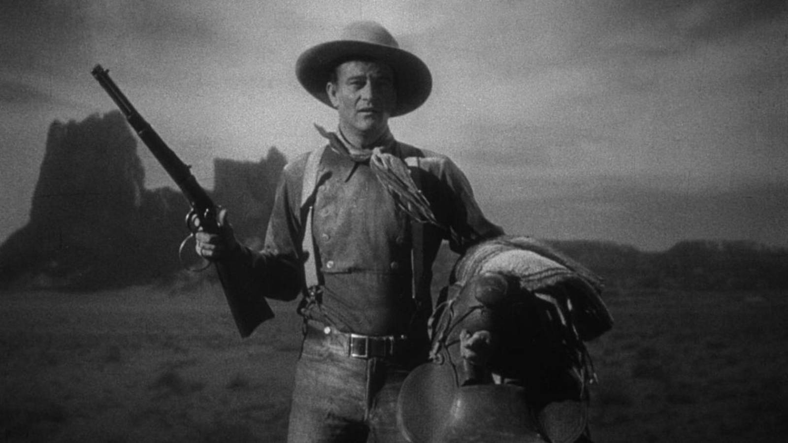 John Wayne holds a gun and saddle in Stagecoach